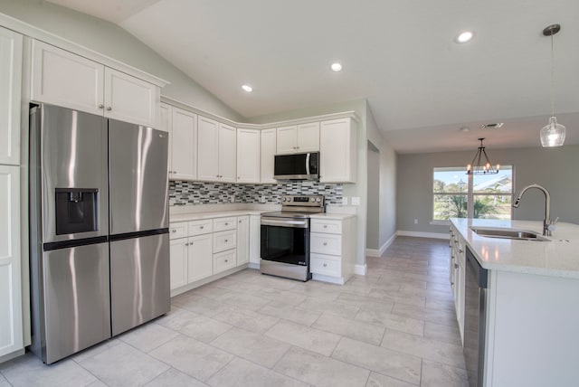 kitchen with appliances with stainless steel finishes, vaulted ceiling, sink, decorative light fixtures, and white cabinets