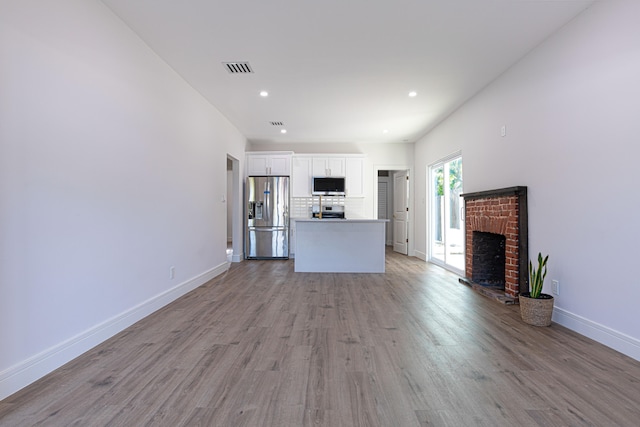 unfurnished living room featuring light wood-type flooring and a brick fireplace