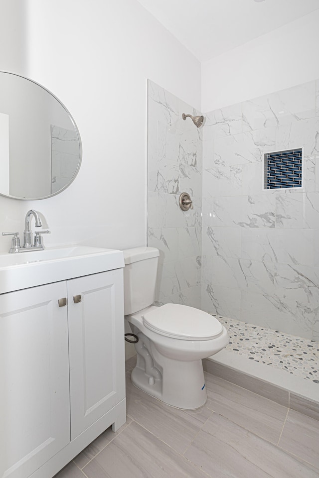 bathroom with toilet, tile floors, vanity, and a tile shower