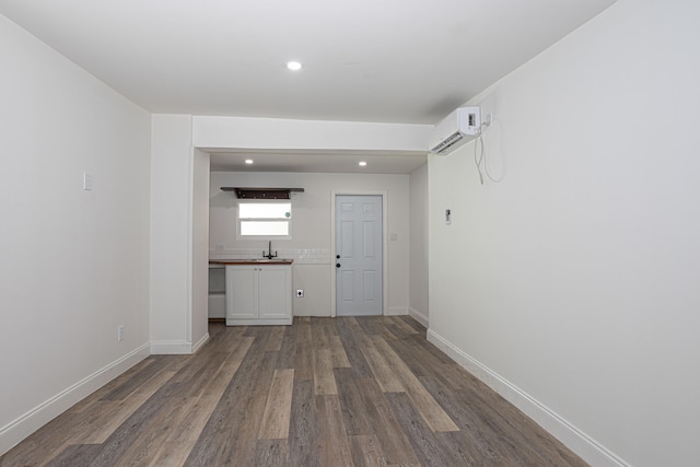 unfurnished living room featuring sink, a wall unit AC, and hardwood / wood-style flooring