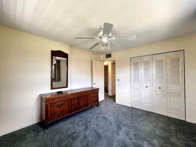 unfurnished bedroom featuring ceiling fan, dark carpet, a textured ceiling, and a closet