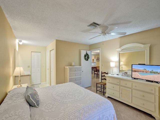 bedroom featuring ceiling fan, light tile patterned floors, and a textured ceiling