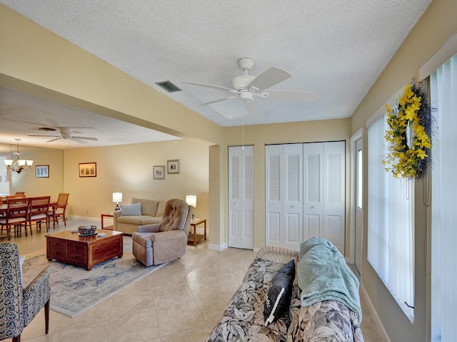 tiled living room featuring ceiling fan with notable chandelier and a textured ceiling