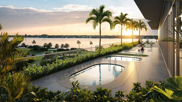 pool at dusk featuring a patio and a water view