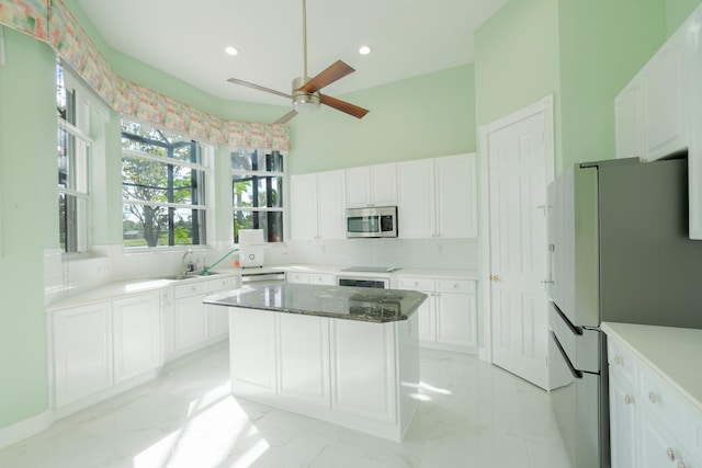 kitchen with a center island, dark stone countertops, white cabinets, stainless steel appliances, and backsplash