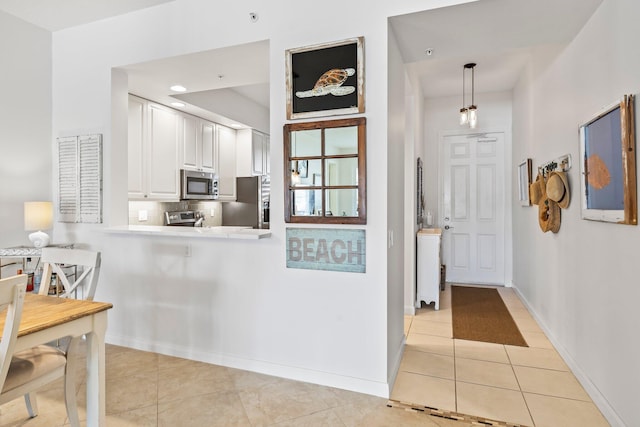 kitchen with hanging light fixtures, stainless steel appliances, white cabinets, and light tile patterned flooring