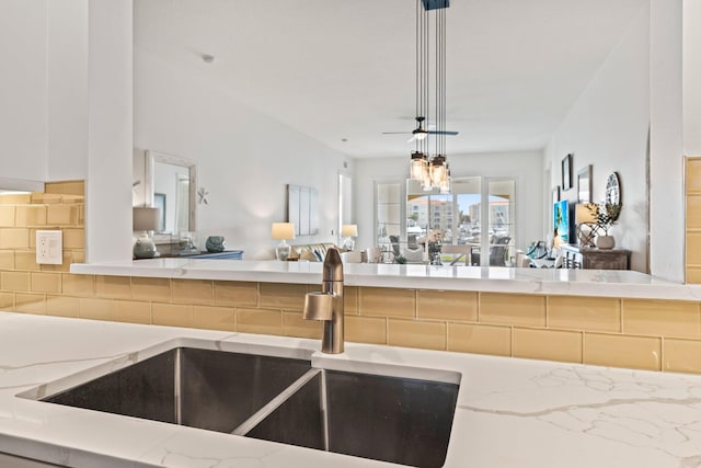 kitchen with pendant lighting, sink, backsplash, light stone counters, and an inviting chandelier