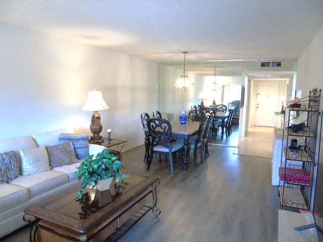 living area with a textured ceiling, wood finished floors, visible vents, and a chandelier