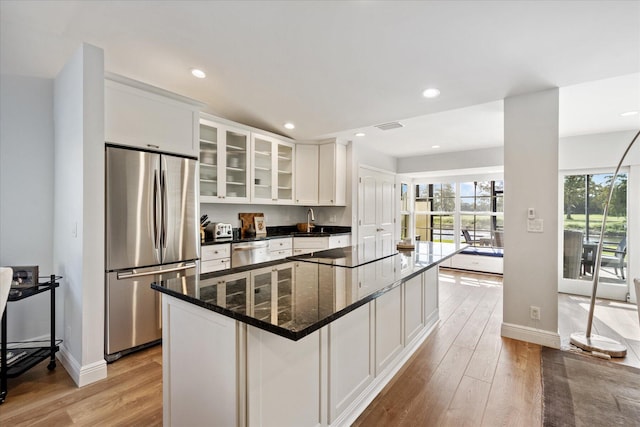 kitchen with light hardwood / wood-style flooring, white cabinetry, appliances with stainless steel finishes, a kitchen island, and dark stone countertops