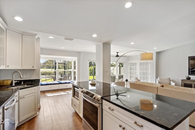 kitchen featuring white cabinets, stainless steel appliances, sink, a kitchen island, and dark stone counters