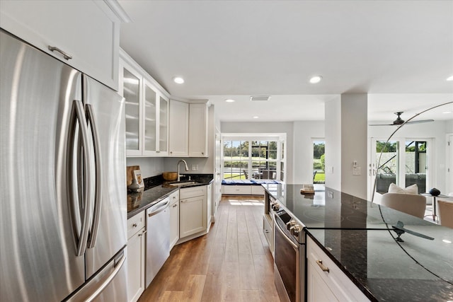 kitchen with stainless steel appliances, light hardwood / wood-style floors, dark stone counters, white cabinets, and sink