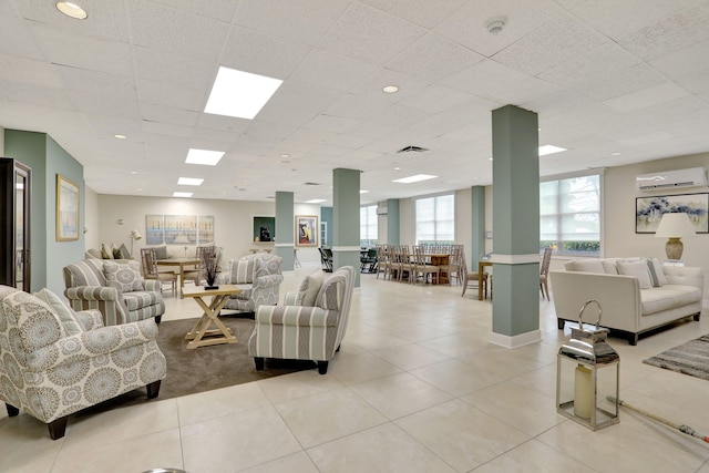 living room featuring a wall mounted AC, a drop ceiling, and light tile patterned floors