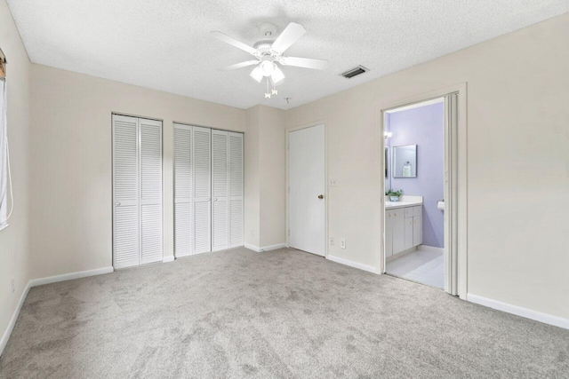 unfurnished bedroom with ensuite bath, ceiling fan, a textured ceiling, light carpet, and two closets