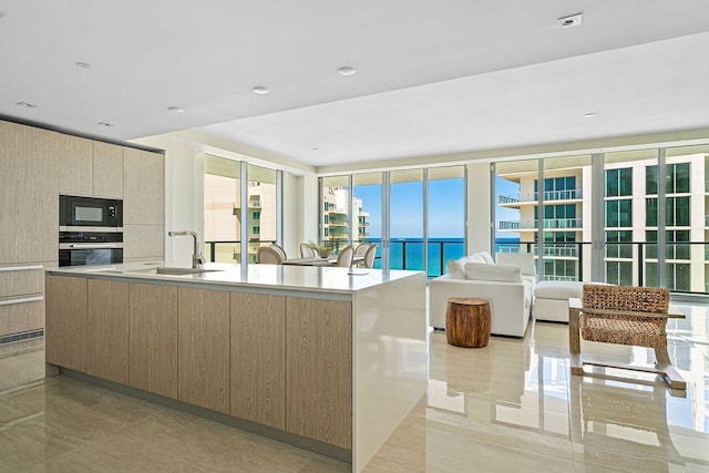 kitchen featuring expansive windows, a water view, oven, a kitchen island with sink, and sink