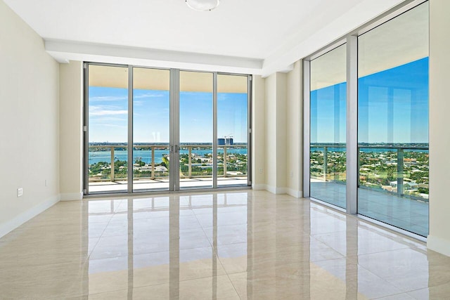 empty room with a water view, a wall of windows, and light tile floors