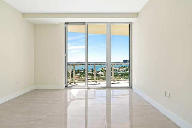 unfurnished room with plenty of natural light, light tile floors, and a water view