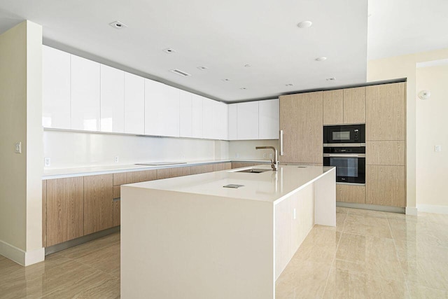 kitchen with a kitchen island with sink, sink, light tile flooring, and white cabinetry