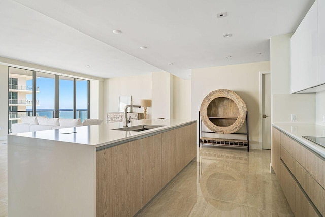 kitchen with white cabinets, expansive windows, a water view, a center island with sink, and sink