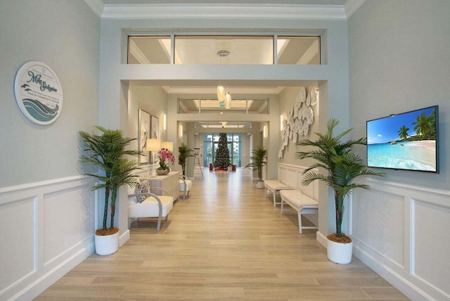 hallway featuring light wood-type flooring, crown molding, and a decorative wall