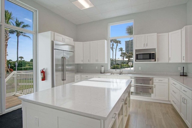 kitchen with a center island, built in appliances, light wood-style flooring, white cabinets, and a sink