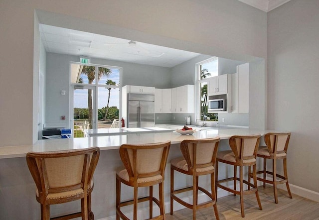 kitchen with a kitchen bar, appliances with stainless steel finishes, a peninsula, white cabinets, and light countertops