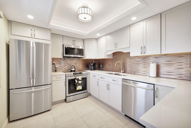 kitchen with a tray ceiling, a sink, stainless steel appliances, light countertops, and backsplash