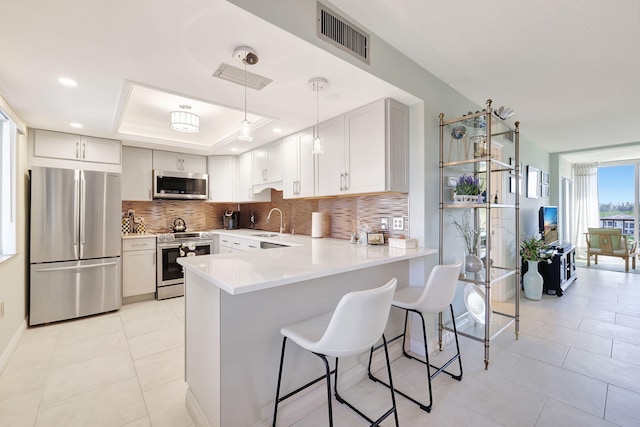 kitchen with visible vents, a tray ceiling, a peninsula, stainless steel appliances, and tasteful backsplash