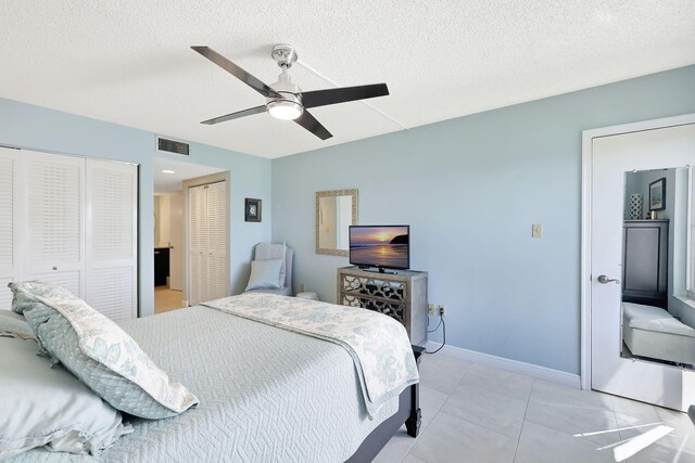 bedroom with light tile patterned floors, a textured ceiling, two closets, and ceiling fan