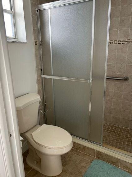 bathroom with a shower with door, toilet, and tile flooring