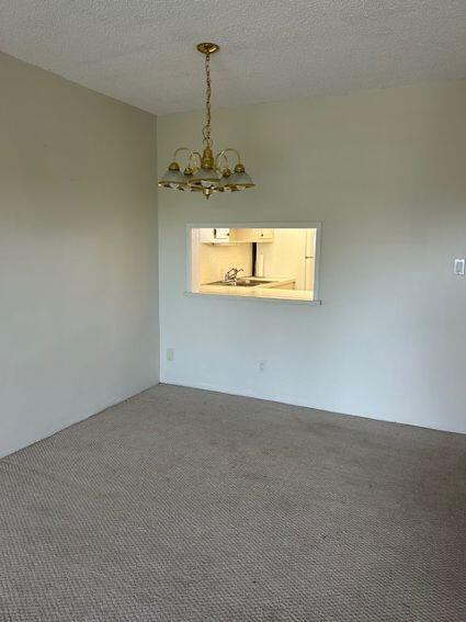 carpeted spare room featuring a chandelier and a textured ceiling