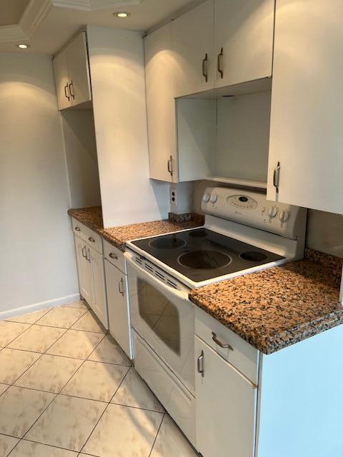 kitchen featuring light tile floors, white range with electric cooktop, white cabinetry, and dark stone counters