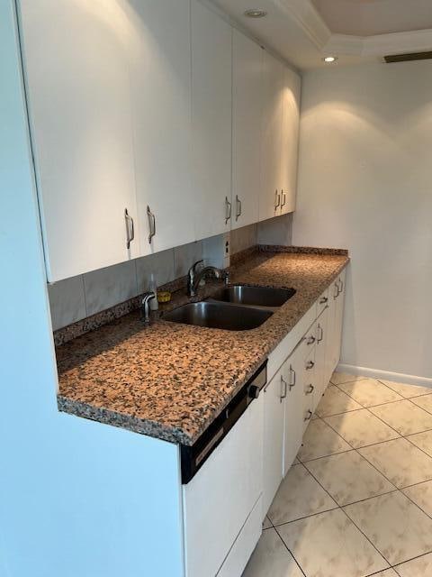 kitchen featuring white dishwasher, light tile flooring, dark stone counters, white cabinetry, and sink