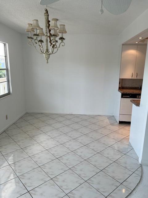 unfurnished dining area featuring a textured ceiling, light tile flooring, and a chandelier