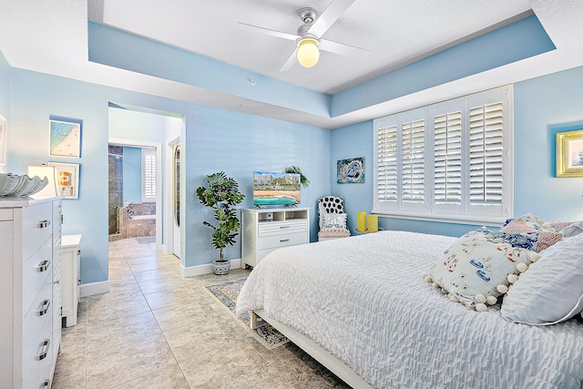 bedroom featuring connected bathroom, light tile patterned floors, ceiling fan, and a tray ceiling