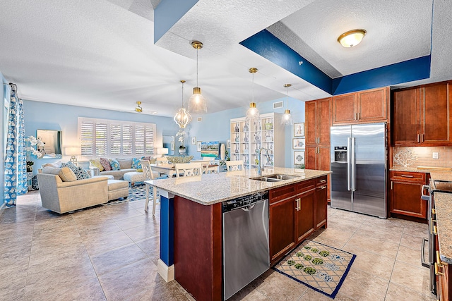 kitchen featuring sink, light stone counters, decorative light fixtures, an island with sink, and stainless steel appliances