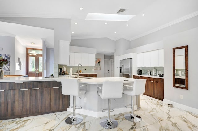 kitchen with stainless steel fridge, vaulted ceiling with skylight, white cabinets, and a breakfast bar area