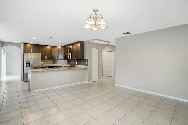 kitchen with dark brown cabinetry, stainless steel appliances, an inviting chandelier, kitchen peninsula, and light tile patterned floors