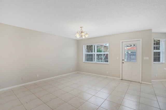 tiled spare room with a chandelier and a textured ceiling