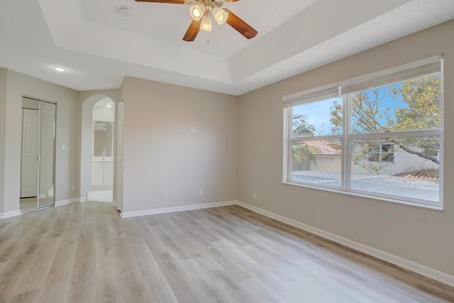 spare room featuring a raised ceiling, ceiling fan, and light hardwood / wood-style flooring