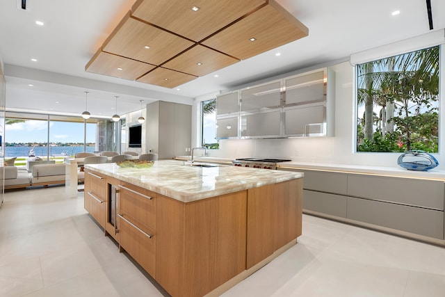 kitchen featuring light stone counters, a healthy amount of sunlight, a kitchen island with sink, and light tile flooring