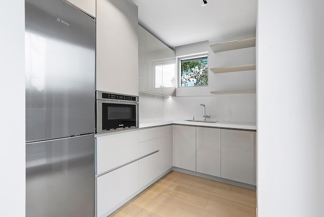 kitchen featuring stainless steel appliances, tasteful backsplash, white cabinets, sink, and light wood-type flooring