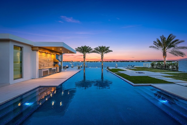 pool at dusk with a patio, area for grilling, and a lawn