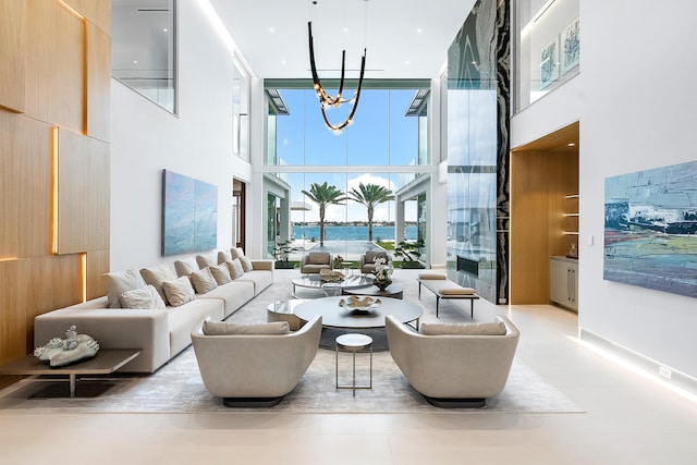 living room featuring a towering ceiling, a water view, a wall of windows, a notable chandelier, and light tile floors