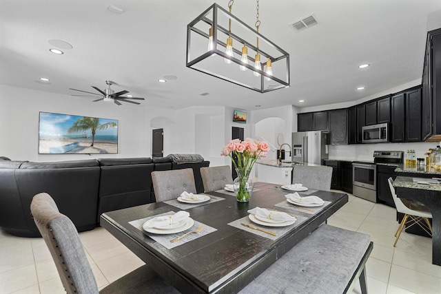 tiled dining area featuring sink and ceiling fan with notable chandelier