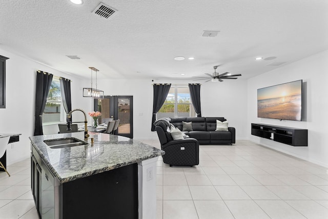 kitchen featuring sink, light stone counters, hanging light fixtures, a textured ceiling, and a kitchen island with sink