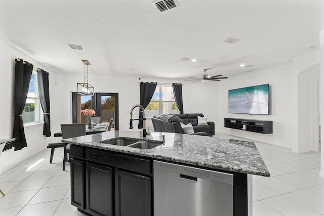 kitchen with sink, hanging light fixtures, a kitchen island with sink, stainless steel dishwasher, and a textured ceiling