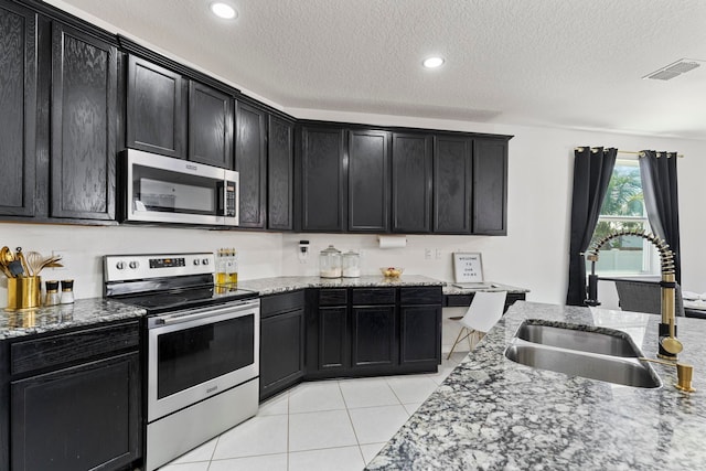 kitchen with light tile patterned flooring, sink, light stone counters, a textured ceiling, and stainless steel appliances