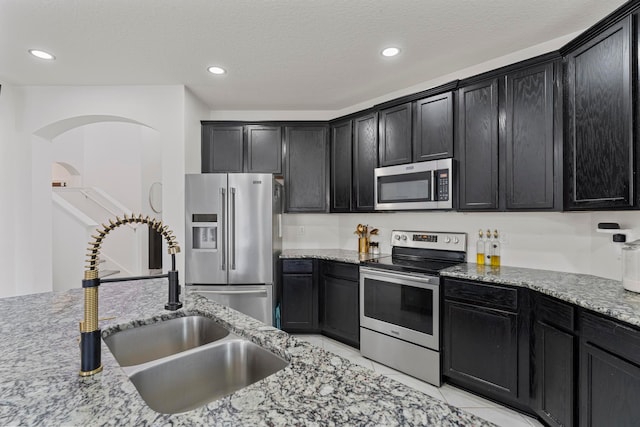 kitchen featuring appliances with stainless steel finishes, sink, a textured ceiling, and light stone counters