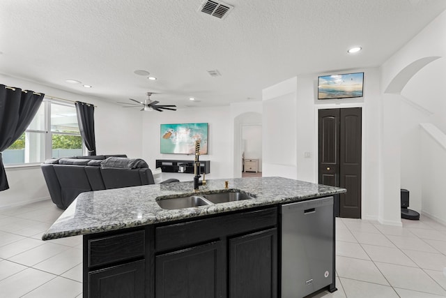 kitchen with sink, light stone counters, light tile patterned floors, stainless steel dishwasher, and an island with sink