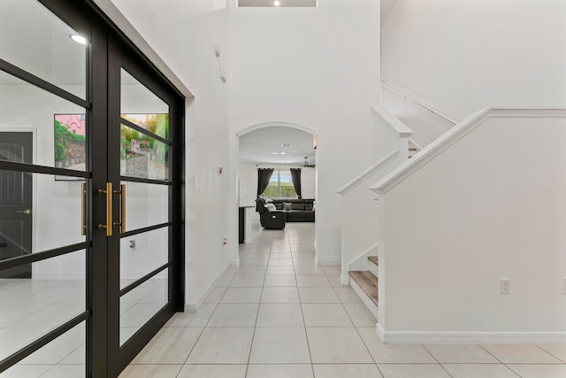 hall featuring light tile patterned floors, a towering ceiling, and french doors